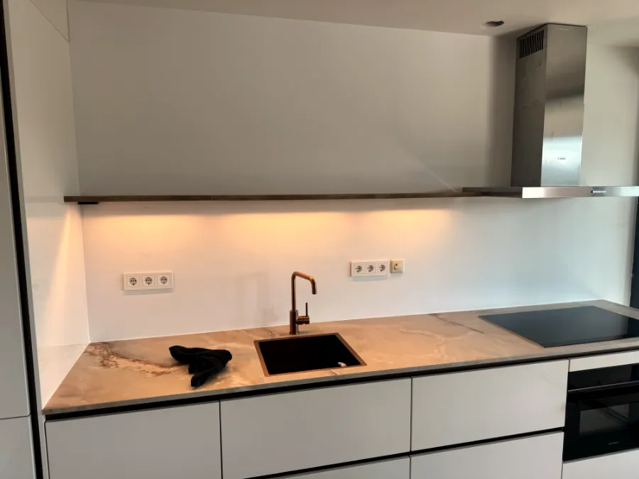 Witte greeploze keuken met koperen kraan en verlichting onder de plank