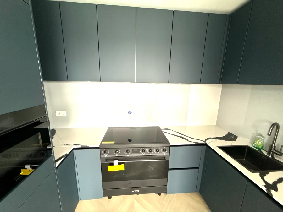 Blauwe U-keuken met fornuis en glazen achterwand