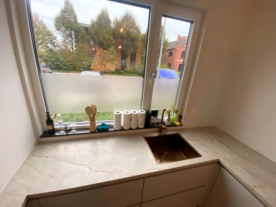 U-keuken met natuursteenlook werkblad en koperen spoelbak bij het raam
