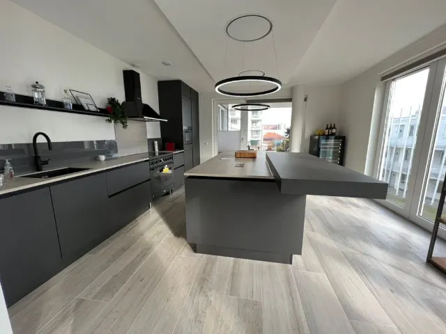 Antraciet keuken met kookeiland en een blad in betonlook