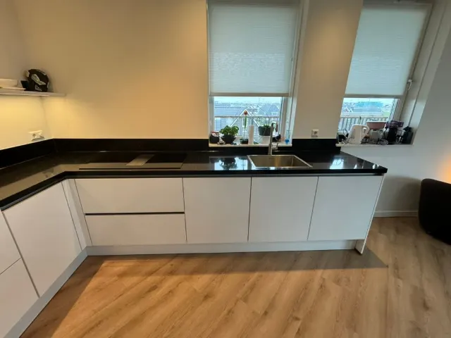 Witte hoogglans keuken in een L-opstelling met zwart werkblad onder het raam