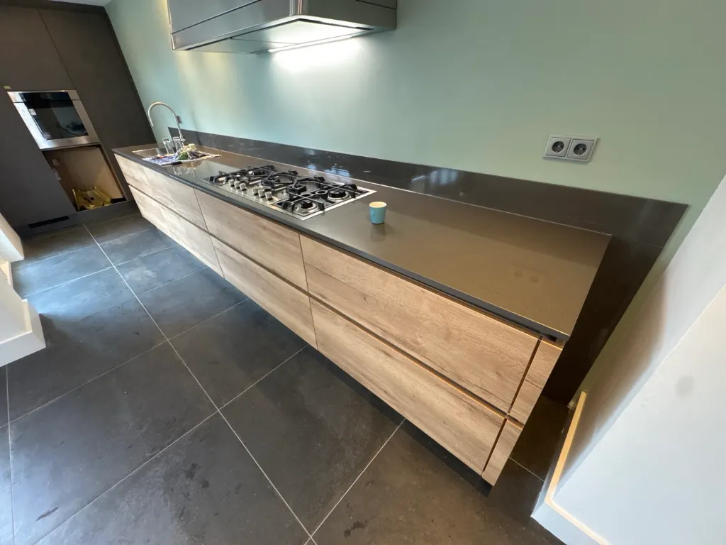 Lange keuken met houten fronten, donker werkblad en gaskookplaat