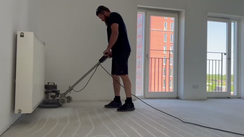 Monteur schuurt de dekvloer vlak met de vloerschuurmachine